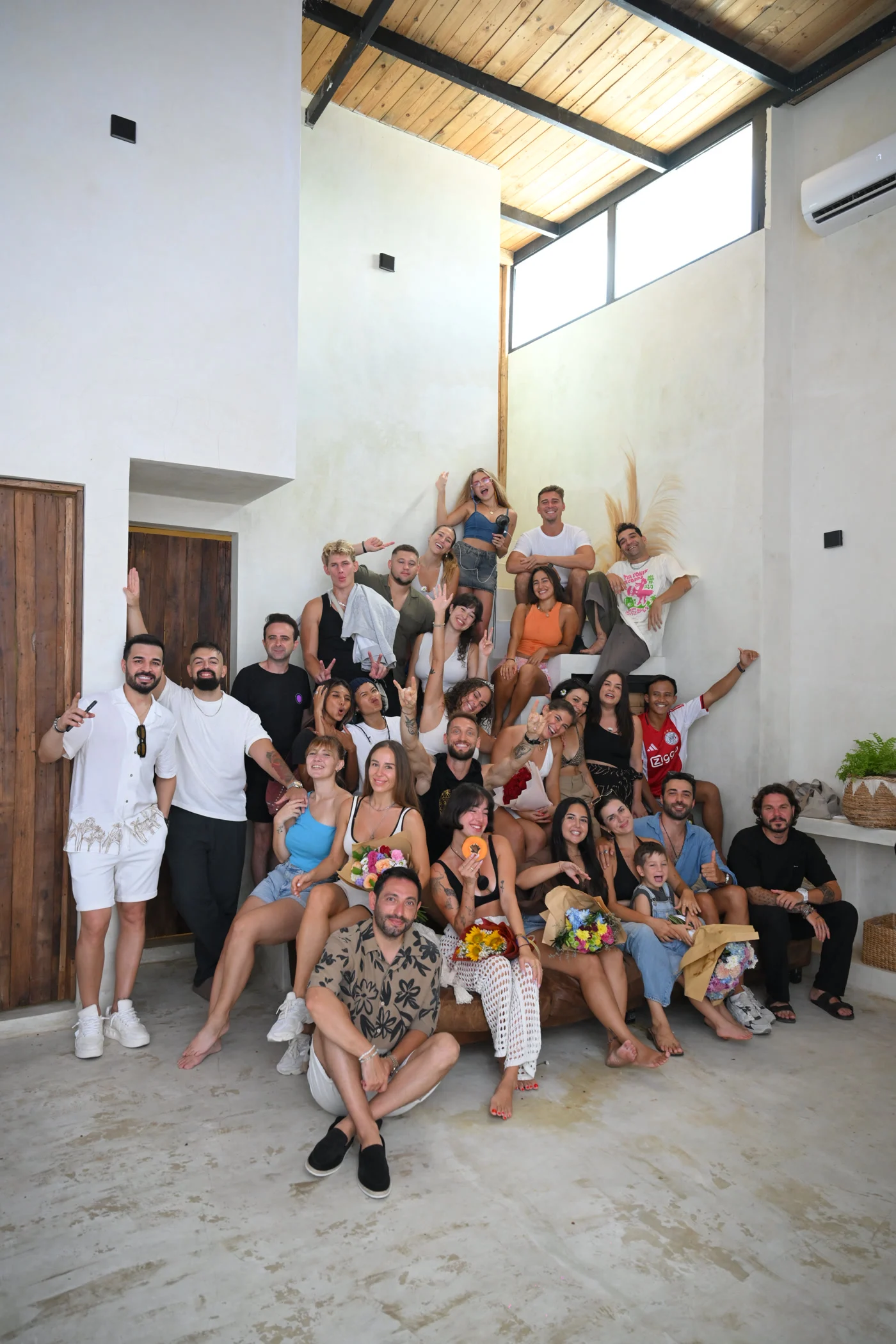 The whole crew, still smiling at the end. That's the goal. Group photo of everyone at an alcohol-free birthday party in Bali, dozens of friends smiling and waving
