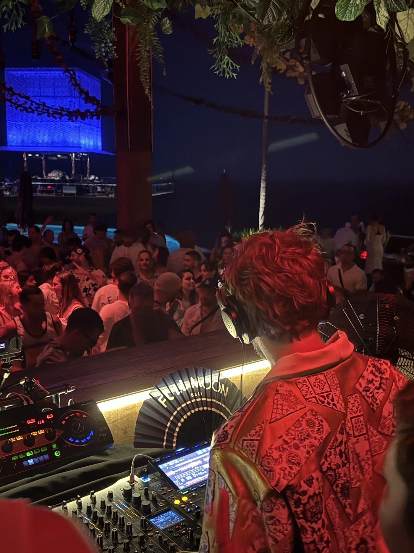 My buddy Kiko working a packed room at Savaya. Same view, different booth. DJ Kiko with red hair and headphones in the booth, facing a packed crowd at Savaya