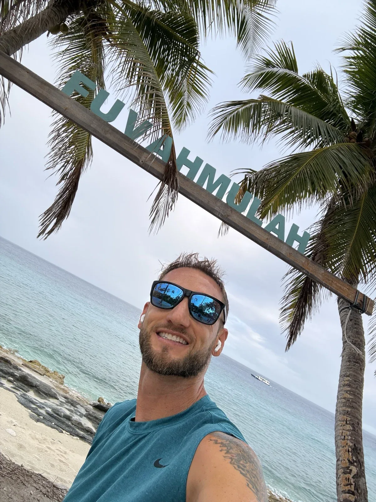 Made it! The Fuvahmulah sign, the palms, and a whole lot of ocean. Zac Spowart arriving in Fuvahmulah, Maldives for tiger shark diving, sober travel adventure, Nomadic Addictt.